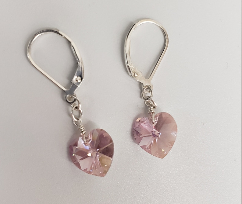May include: A pair of silver dangle earrings with a light purple heart-shaped crystal charm.