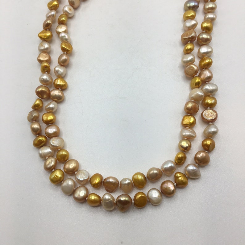 K&ouml;nnte beinhalten: Eine doppelreihige Perlenkette mit goldenen und cremefarbenen Perlen.