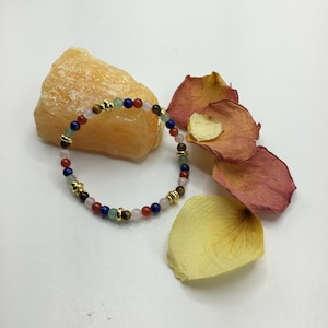 May include: A multi-colored beaded bracelet with gold accents. The bracelet features various gemstone beads, including green, blue, pink, and brown.