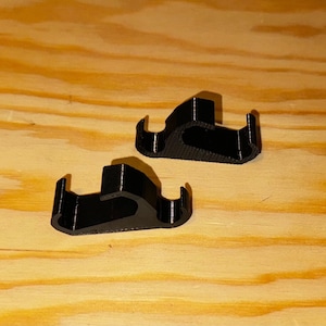 May include: Two black plastic hooks, designed to hang items on a wall or other surface.