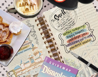 May include: A notebook with a hand-drawn illustration of a castle and the words "the Smell" circled. The notebook has a list of words including "looting scallywags", "happy haunts", "jambalaya jazz", "stretching portraits", and "powdered mickeys". A guide map for Disneyland is in the foreground.