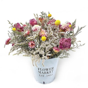 Peut inclure: Un bouquet de fleurs séchées dans des tons de rose, blanc et jaune, disposé dans un seau en métal blanc avec le texte "Flower Market Est. 1953".