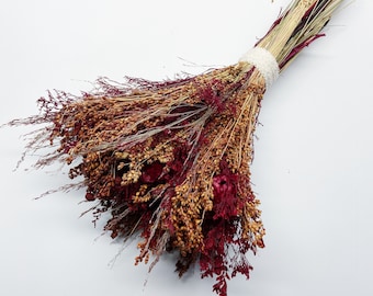 May include: A bouquet of dried flowers with brown and red hues. The flowers are tied together with a white ribbon.