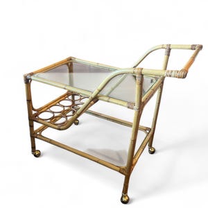 May include: A vintage bamboo bar cart with a glass top and lower shelf. The cart has a built-in bottle holder and is mounted on small caster wheels. The bamboo has a natural, light brown color.