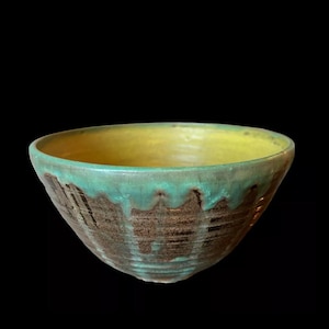 May include: A ceramic bowl with a yellow glaze on the inside and a green and brown glaze on the outside. The bowl has a textured surface.