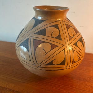 May include: A brown ceramic vase with a geometric design in black, brown, and green. The vase has a round body and a narrow opening.