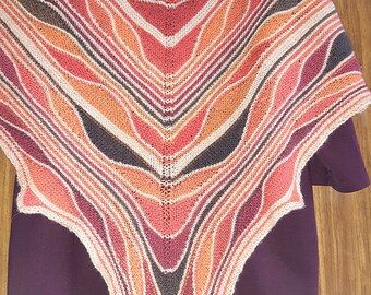 Puede incluir: Un chal triangular tejido en un patrón de rayas coloridas con tonos de naranja, rojo, marrón y blanco.