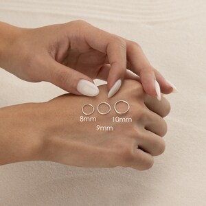 A person's hand is shown wearing three different sizes of rings on the fingers, with the largest ring being 8mm, the medium-sized ring being 10mm, and the smallest ring being 9mm.