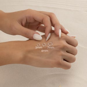 A close-up image of a person's hand wearing three different sizes of rings on the fingers.