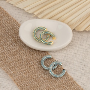 May include: Two pairs of C-shaped hoop earrings, one pair in gold-tone metal and one pair in silver-tone metal. Each earring features a continuous row of small, bright turquoise blue stones embedded along the outer surface of the curved band.