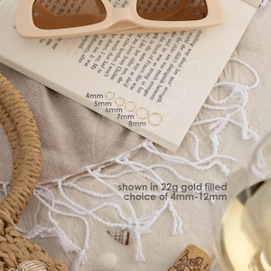 a pair of sunglasses, a book, a wine glass, and some seashells arranged on a table.
