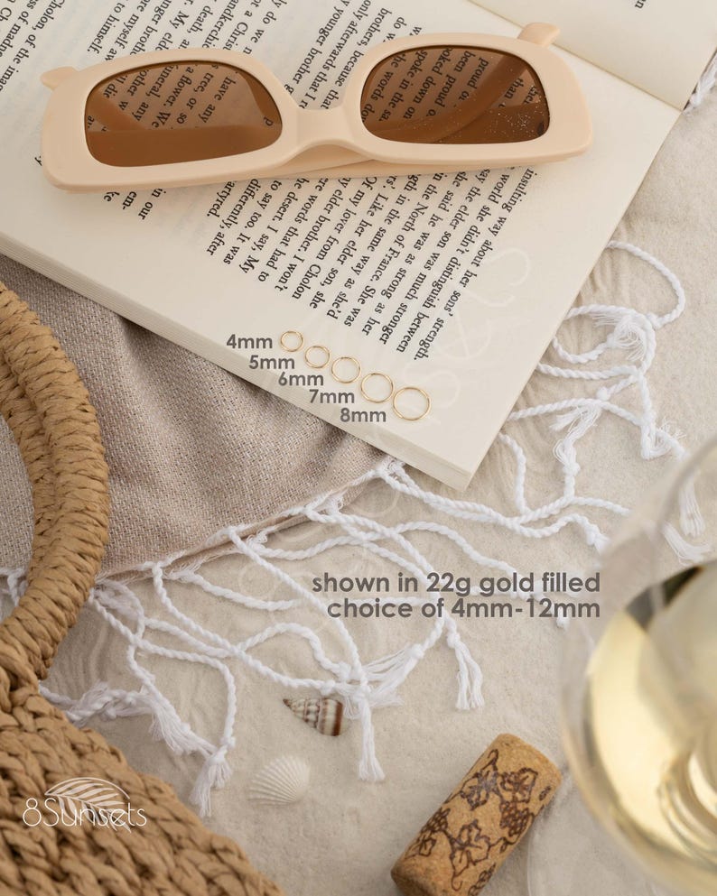 a pair of sunglasses, a book, a wine glass, and some seashells arranged on a table.