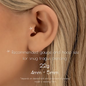 May include: Close-up of an ear with a gold-colored hoop earring featuring a starburst design with small, clear stones. The text recommends a 22g gauge and 4mm-5mm hoop size for a snug tragus piercing.