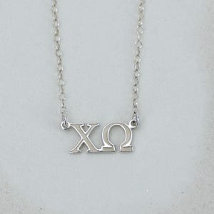 May include: A silver-toned necklace featuring a pendant with the Greek letters Chi and Omega. The pendant is attached to a delicate silver-toned chain with small circular links. The metal has a polished finish that reflects light evenly.