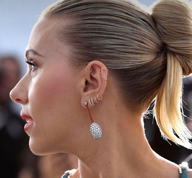 May include: A close-up of a person's ear with multiple gold hoop earrings and a single diamond earring. The earrings are in the shape of circles and are arranged in a row. The diamond earring is at the bottom of the row and is the largest of the earrings.