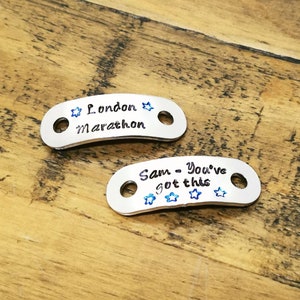 May include: Two silver metal tags with blue star accents. The first tag reads "London Marathon" and the second tag reads "Sam - You've got this".