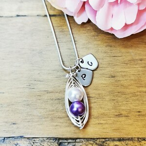 May include: A silver necklace with a pea pod charm containing three pearls. The pearls are white and purple. The necklace also has two silver heart charms with the letters 'P' and 'C' on them.
