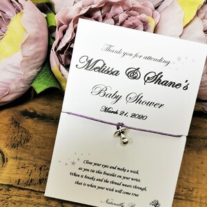 May include: A white card with purple string attached to a silver baby rattle charm. The card says "Thank you for attending Melissa & Shane's Baby Shower March 21, 2020" and includes a poem about making a wish on the bracelet.