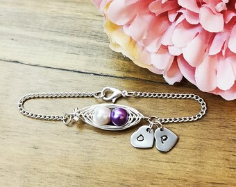 May include: A silver chain bracelet with a purple and white pearl pea pod charm and two silver heart charms with the letters "D" and "P" engraved on them.