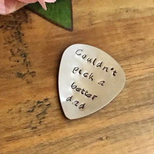 Puede incluir: Púa de guitarra plateada con las palabras "Couldn't pick a better dad" grabadas en ella.
