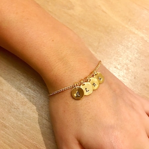 May include: A gold chain bracelet with five gold charms, each with a letter engraved on it. The letters are A, L, N, and two more letters that are not visible in the image.