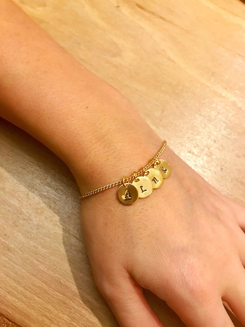 May include: A gold chain bracelet with five gold charms, each with a letter engraved on it. The letters are A, L, N, and two more letters that are not visible in the image.