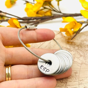 May include: A silver keychain with a cable chain and a stack of round metal tags. The top tag has the letters "ESP" engraved on it.