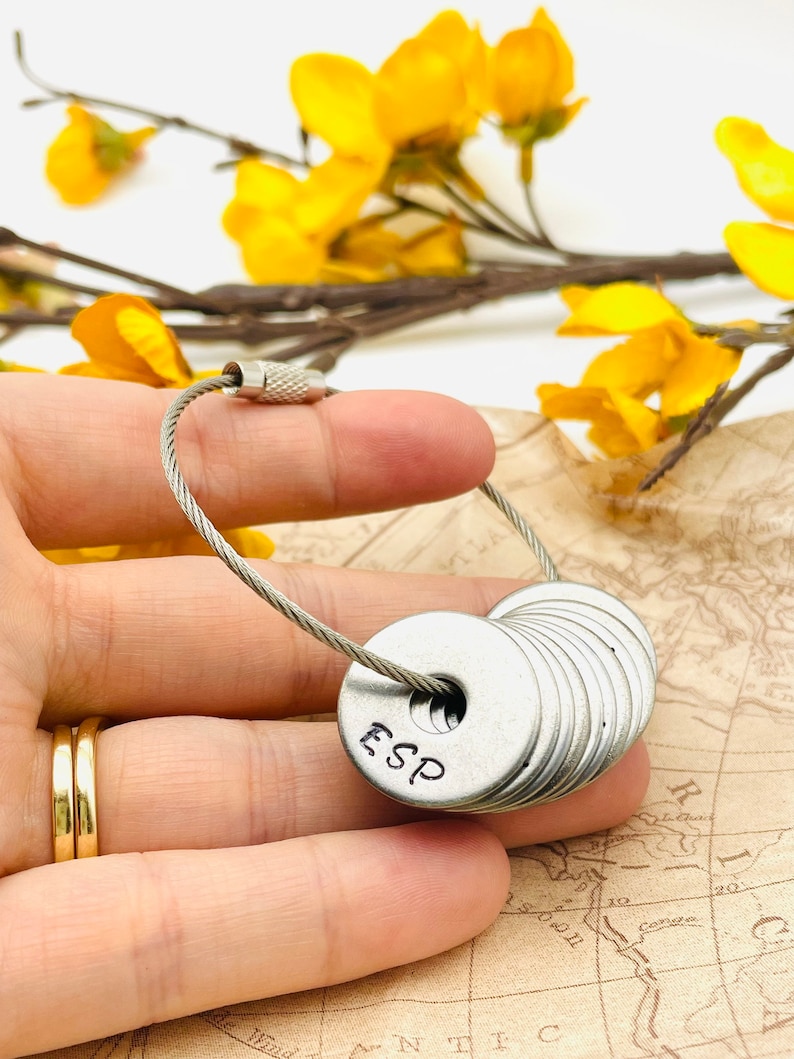 May include: A silver keychain with a cable chain and a stack of round metal tags. The top tag has the letters "ESP" engraved on it.