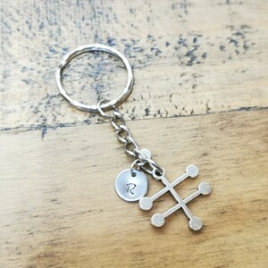 Puede incluir: Llavero de plata con un peque&ntilde;o charm redondo con la letra "R" y un dise&ntilde;o geom&eacute;trico con seis c&iacute;rculos.