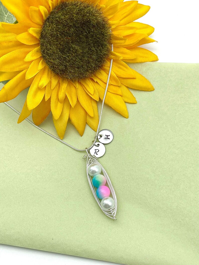 Puede incluir: Un collar de plata con un dije en forma de vaina de guisante con tres perlas de colores en su interior. El collar tambi&eacute;n tiene dos dijes de plata con las letras "R" y "H" en ellos.
