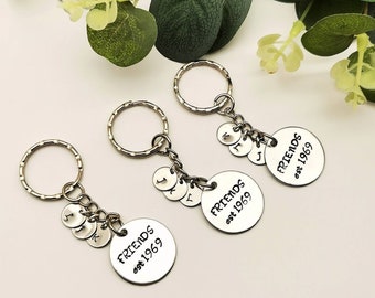 May include: Three silver keychains with the word "FRIENDS" and the year "est. 1969" engraved on each. Each keychain has a small silver charm with a letter on it.
