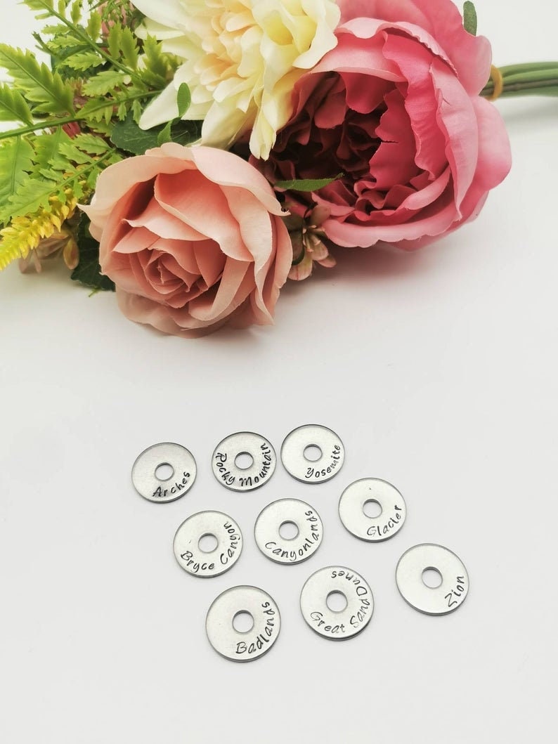 May include: Ten silver metal discs with different national park names engraved on them. The names include Arches, Rocky Mountain, Yosemite, Bryce Canyon, Canyonlands, Glacier, Badlands, Great Sand Dunes, and Zion.