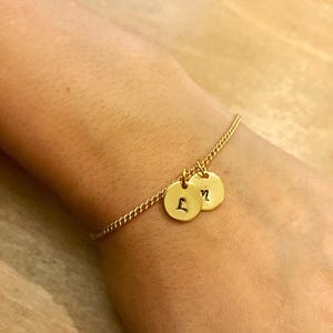 May include: A gold chain bracelet with two round charms, each engraved with a letter. The charms are 'L' and 'N'.