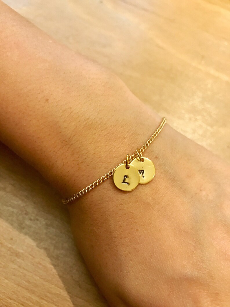 May include: A gold chain bracelet with two round charms, each engraved with a letter. The charms are 'L' and 'N'.