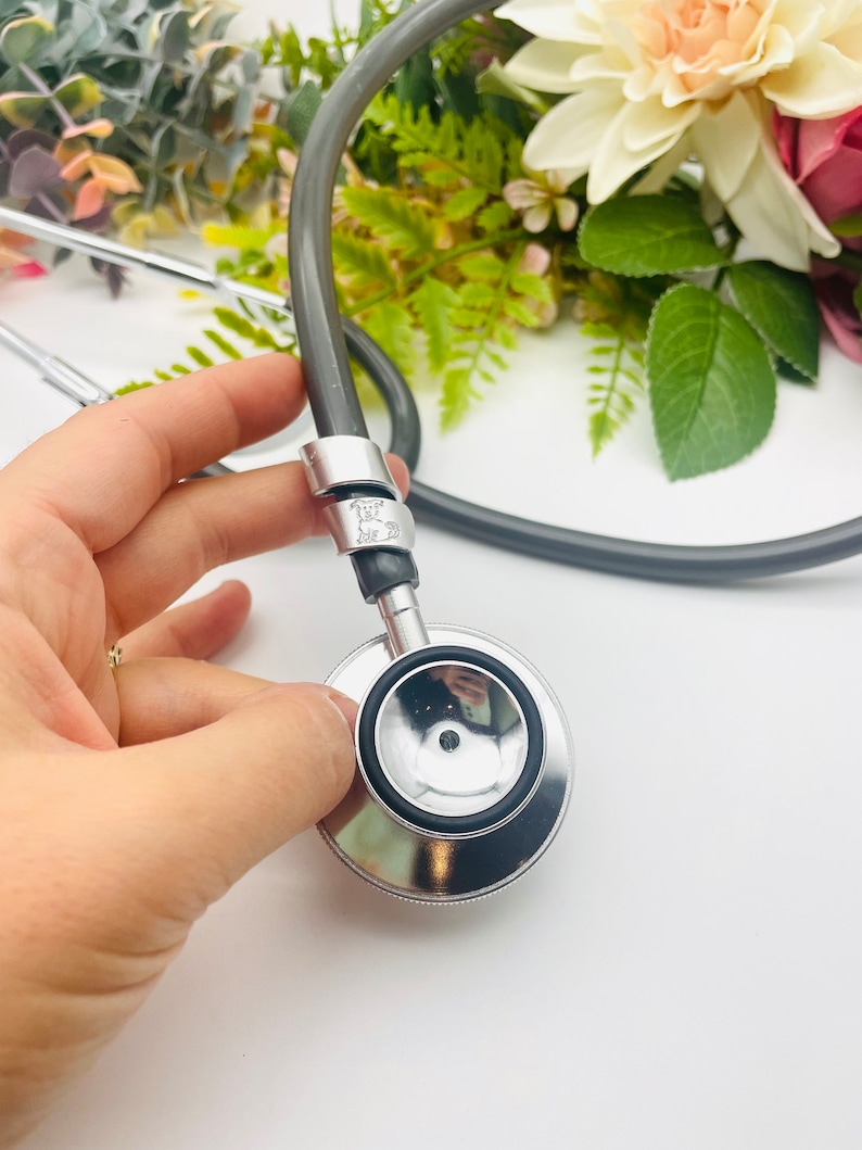 May include: A silver stethoscope with a black rubber tube and a silver earpiece. The stethoscope has a silver ring with the text "Joe 20" engraved on it.