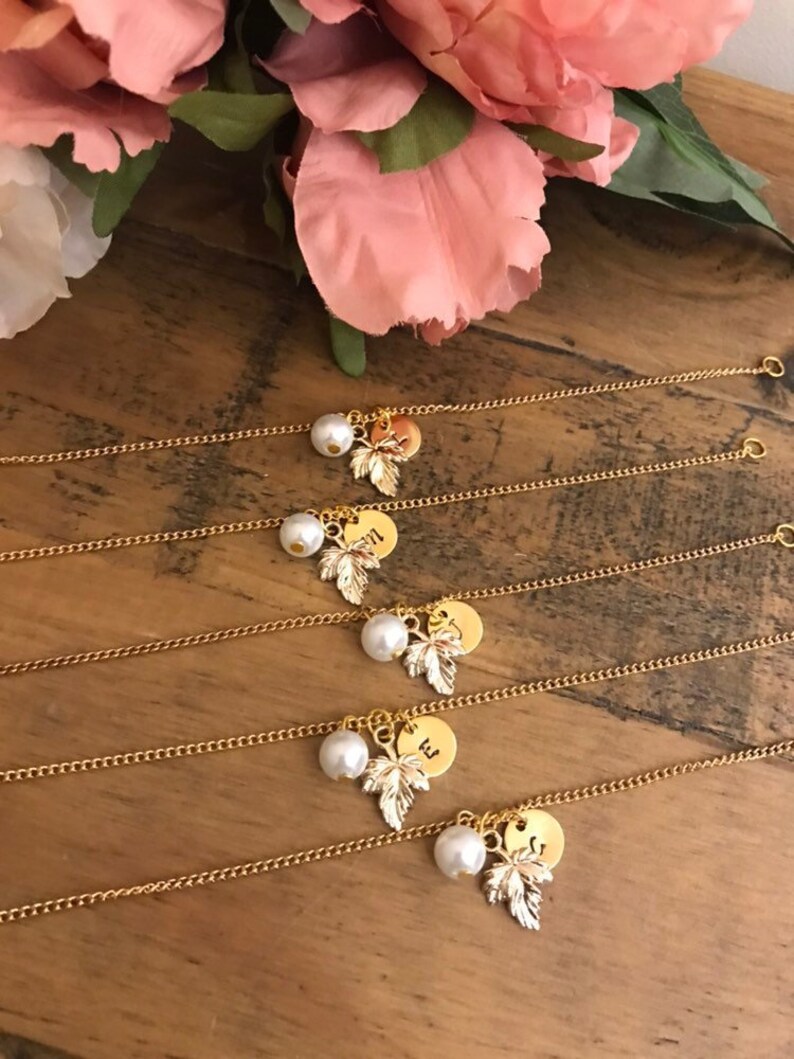 May include: Four gold chain bracelets with a pearl and leaf charm. Each charm has a letter on it, spelling out the word "will".