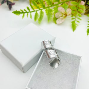 May include: A silver metal ring with the word "Gwen" engraved on it. The ring is in a white box.