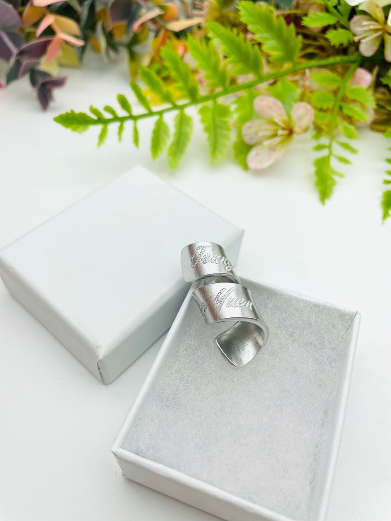 May include: A silver metal ring with the word "Gwen" engraved on it. The ring is in a white box.