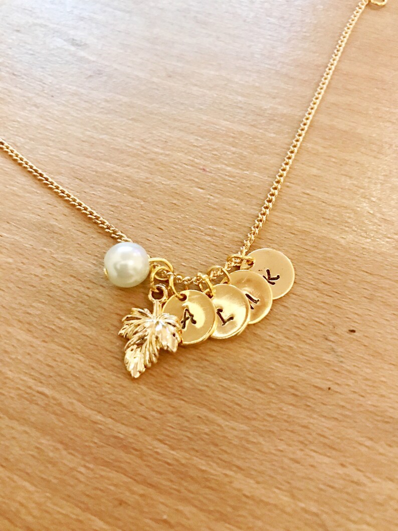 May include: Gold necklace with a pearl charm, a leaf charm, and five small round charms with letters on them. The letters are A, L, I, K, and L.