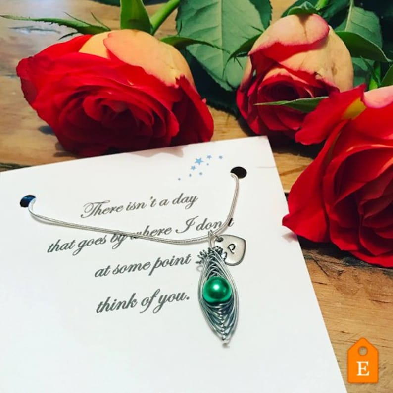 May include: A silver necklace with a green pearl charm and a heart charm with the letter "P" engraved on it. The necklace is displayed on a white card with the text "There isn't a day that goes by where I don't at some point think of you."
