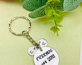 May include: Silver keychain with a round charm that says "FRIENDS est 2011". There are two smaller charms with the letters "H" and "R" on them.