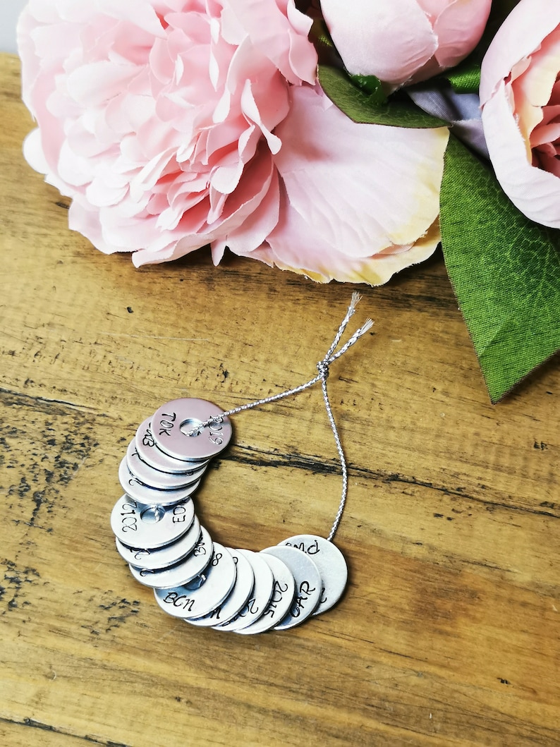 May include: A silver charm bracelet with a string of round metal charms, each with a different word or date engraved on it. The charms are arranged in a circle and are hanging from a silver string.