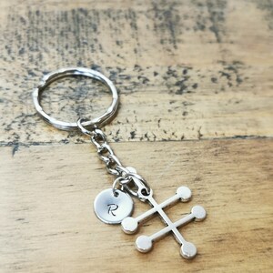 Puede incluir: Llavero de plata con un peque&ntilde;o charm redondo grabado con la letra "R" y un charm m&aacute;s grande con forma de &aacute;rbol estilizado con seis c&iacute;rculos redondos.