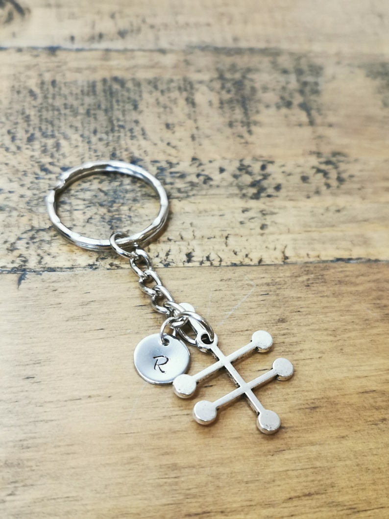 Puede incluir: Llavero de plata con un peque&ntilde;o charm redondo grabado con la letra "R" y un charm m&aacute;s grande con forma de &aacute;rbol estilizado con seis c&iacute;rculos redondos.