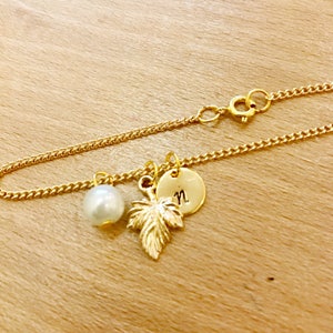 May include: A gold chain bracelet with a pearl charm, a gold leaf charm, and a gold disc charm with the letter "N" engraved on it.