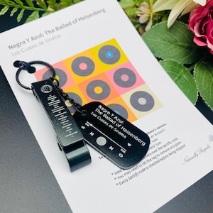 Puede incluir: Llavero de metal negro con un abridor de botellas y una etiqueta de código Spotify. La etiqueta tiene el texto "Negro Y Azul: The Ballad of Heisenberg Los Cuates de Sinaloa".