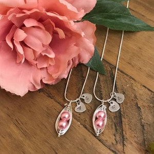 May include: Two silver necklaces with pink pearl pea pod charms and initial heart charms. The charms are engraved with the letters A and G.