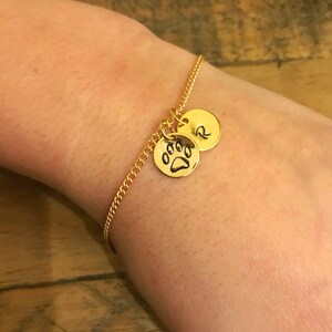 May include: A gold chain bracelet with two charms. One charm is a paw print and the other charm is a letter 'R'.