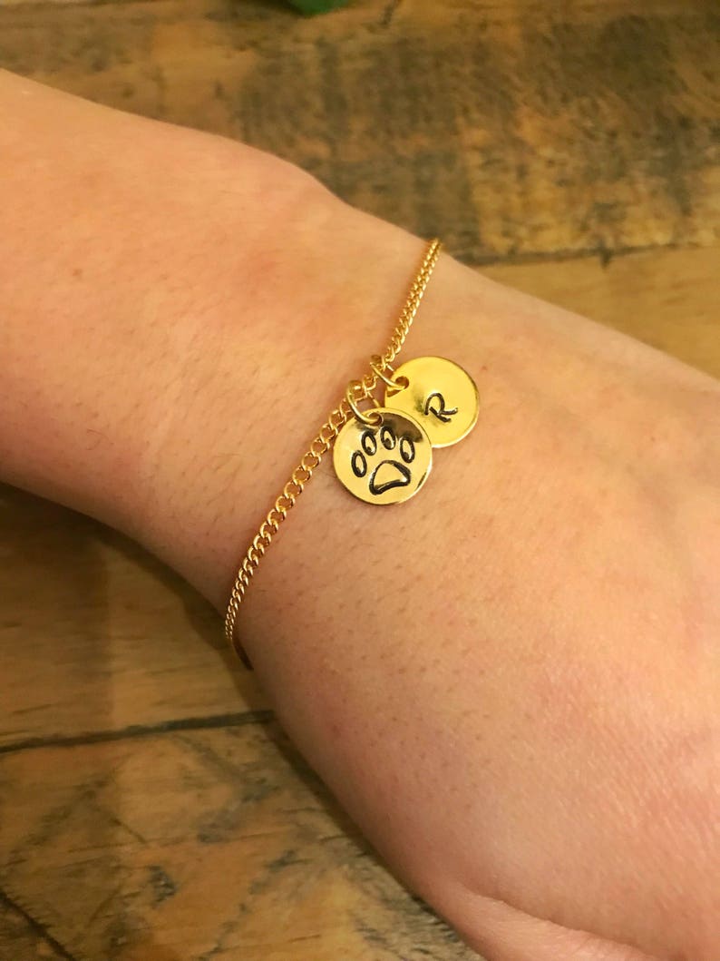May include: A gold chain bracelet with two charms. One charm is a paw print and the other charm is a letter 'R'.