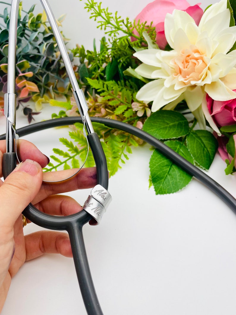May include: A black stethoscope with a silver charm engraved with the names "Alex" and "Nurse".